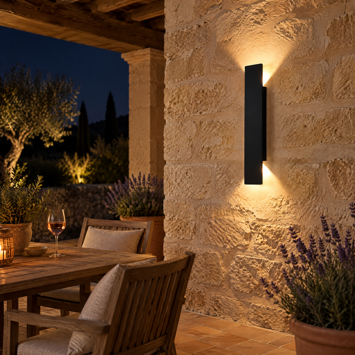 Applique murale extérieur noire sur un mur en pierre d'une terrasse provençale le soir