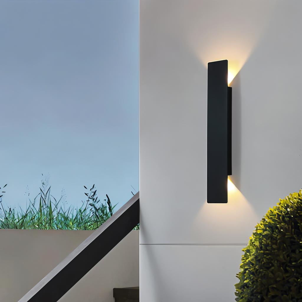 Applique murale extérieur noire allumée sur un mur blanc près d'un escalier