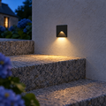 Applique murale extérieure LED carrée noire encastrée éclairant une marche en granit le soir