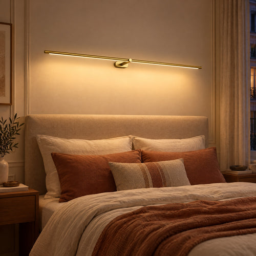Applique murale LED dorée en barre fine allumée au-dessus d'une tête de lit le soir
