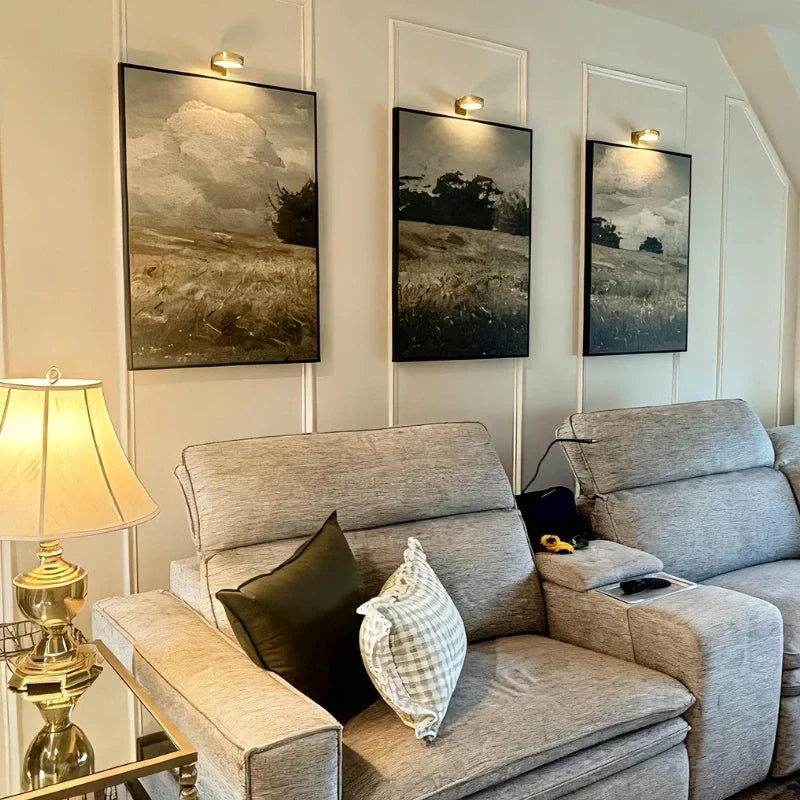 Trois lampes de tableau dorées au-dessus de paysages derrière le canapé