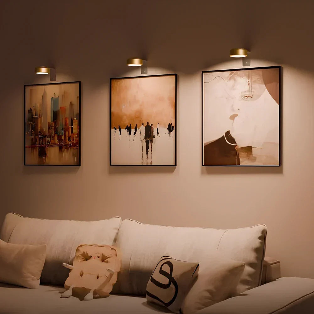 Appliques murales sans fil dorées au-dessus de trois tableaux colorés dans le salon