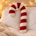 Coussin sucre d'orge en peluche rouge et blanc sur un lit aux draps blancs avec guirlande lumineuse