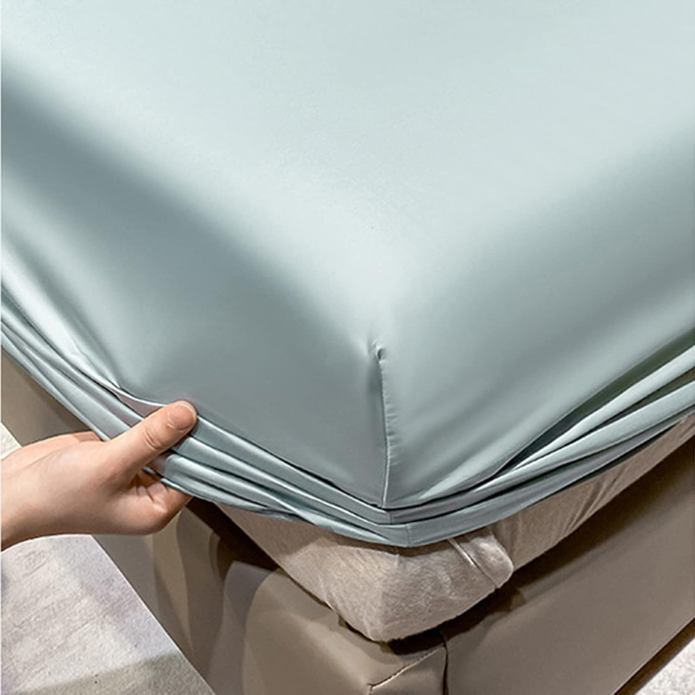 Main ajustant le drap-housse vert menthe sur l'angle du matelas