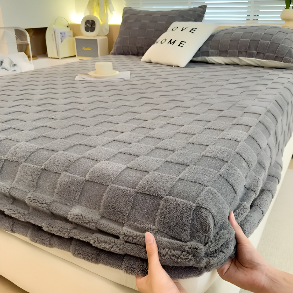 Deux mains glissent le drap-housse gris sur le coin du matelas
