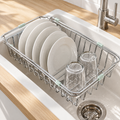 Égouttoir vaisselle extensible en inox posé sur un évier blanc, avec assiettes et verres