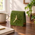 Horloge design à poser vert olive en céramique sur un bureau en noyer, lumière du matin
