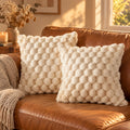 Deux housses de coussin crème à relief bulles sur un canapé en cuir camel au soleil couchant